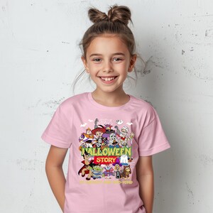 May include: A light pink short-sleeved t-shirt featuring a colorful graphic of various animated characters dressed in Halloween costumes. The text reads HALLOWEEN STORY and TO INFINITY AND BOO-YOND in yellow and green lettering.