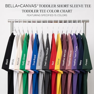 May include: A Bella+Canvas toddler short sleeve tee color chart featuring 15 shirts on white hangers. Colors include black, white, natural, kelly green, pink, true royal, athletic heather, dark grey heather, red, yellow, heather maroon, heather mauve, heather team purple, navy, and forest.