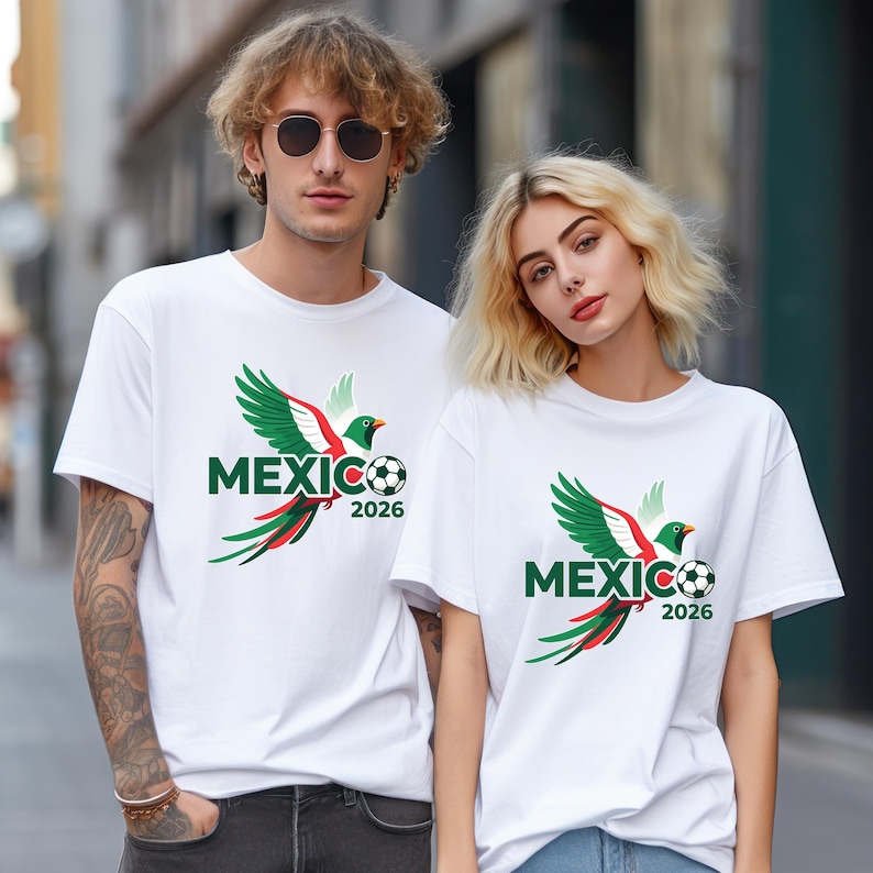 May include: White t-shirts featuring a green, red, and white bird design with the word "MEXICO" and the year "2026" printed in green. The design includes a soccer ball. The shirts are worn by two people.