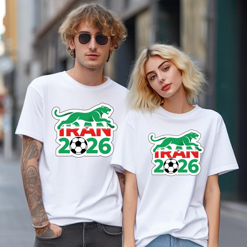May include: White t-shirts with a green panther design above the word "IRAN" in red and white, a soccer ball, and the number "2026". The shirts are worn by two people.