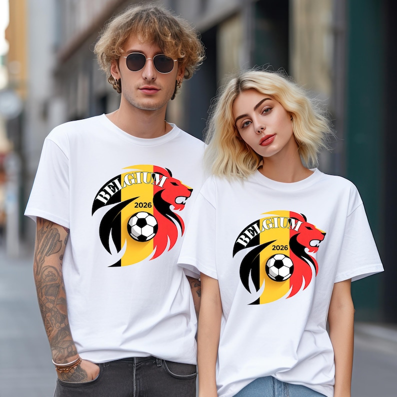 May include: White t-shirts featuring a graphic of a lion's head with the word "BELGIUM" and the year "2026". The lion design incorporates the colors of the Belgian flag and a soccer ball. The shirts are short-sleeved.