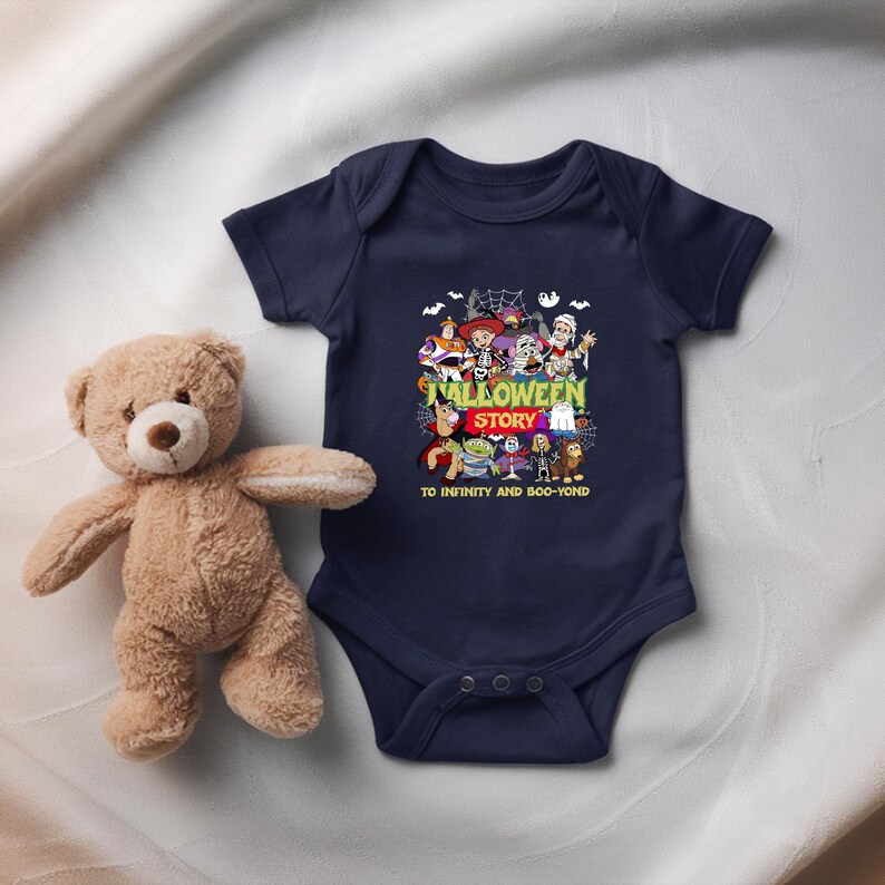 May include: A navy blue short-sleeved baby bodysuit featuring a graphic print of various cartoon characters in Halloween costumes. The text reads HALLOWEEN STORY and TO INFINITY AND BOO-YOND. A light brown plush teddy bear is positioned to the left.