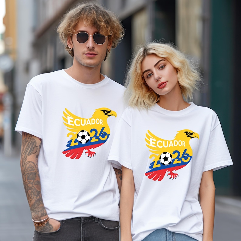 May include: White t-shirts with a yellow eagle design, the word "Ecuador", and the number "26" in blue. A soccer ball is in the center of the design. The eagle has red, yellow, and blue accents. The shirts are worn by two people.