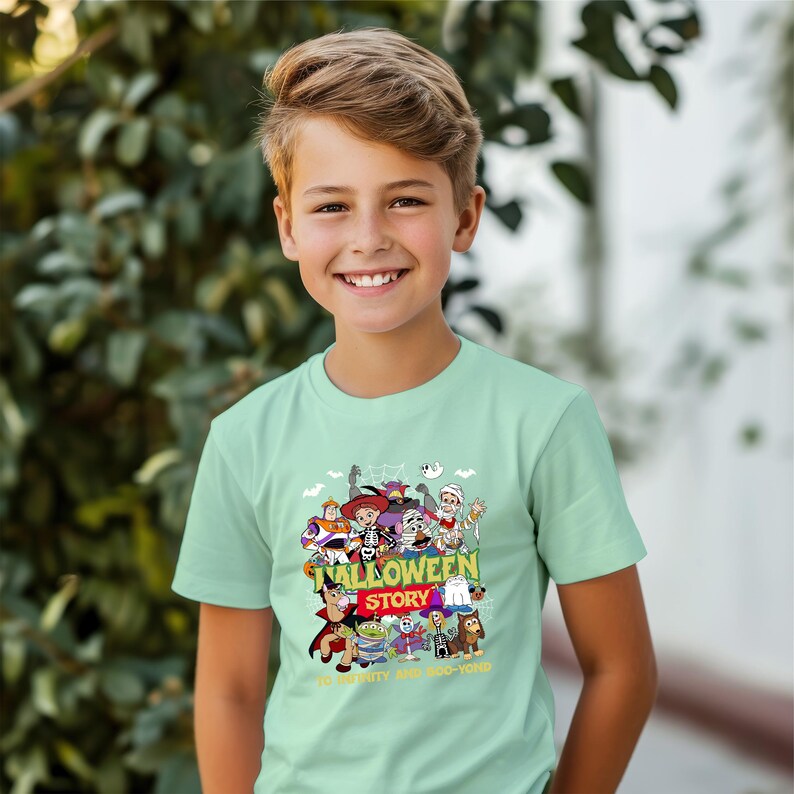 May include: A light mint green short-sleeve t-shirt featuring a colorful graphic print of various animated characters in Halloween costumes. The text reads HALLOWEEN STORY and TO INFINITY AND BOO-YOND with small ghost and spiderweb illustrations.