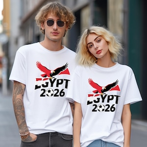 May include: White t-shirts with a graphic design. The design includes a red and black eagle, the word "EGYPT", a football, and the year "2026". The shirts are short-sleeved.