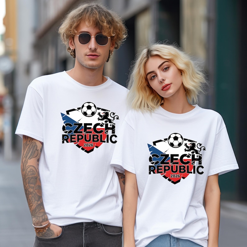 May include: White t-shirts with a Czech Republic soccer design. The design includes a soccer ball, the Czech flag colours, and the text "CZECH REPUBLIC 2026". The shirts are worn by two people.