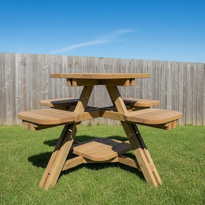 May include: A wooden picnic table with a round top and attached benches. The table is made of light-colored wood and is set on a grassy lawn with a wooden fence in the background. The sky is blue.