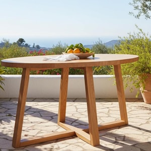 Puede incluir: Mesa ovalada de madera marrón claro, con cuatro patas anguladas y una base en forma de cruz. Un cuenco con naranjas y limones encima, junto con un paño blanco. La mesa está al aire libre en un patio de piedra. La mesa mide unos 120 cm de largo.