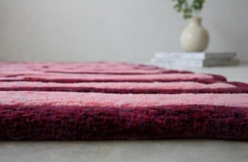 May include: A plush, striped rug in shades of pink and burgundy. The rug has a soft, textured surface with horizontal stripes. The rug is a decorative item for a living room or bedroom.