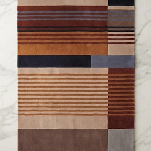 Pode incluir: Um tapete retangular com um padrão geométrico de riscas horizontais e verticais. A paleta de cores inclui tons de bege, castanho-claro, laranja ferrugem, castanho escuro, azul marinho e cinzento ardósia, dispostos em blocos.