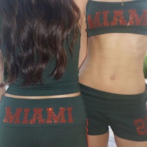 May include: Dark green athletic wear set with the word "MIAMI" in red rhinestones. The set includes a tank top, shorts, and a sports bra. The shorts have the number "2" in red rhinestones.