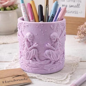 May include: A white ceramic mug with a black handle and the text "But First, Coffee" in a black, handwritten-style font. The mug is on a white surface.