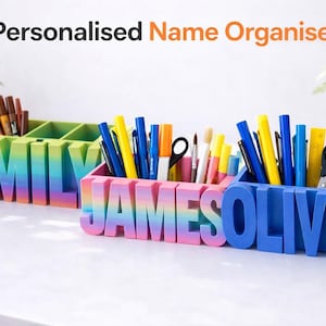 Könnte beinhalten: Personalisierte Namens-Organizer in Regenbogen-, Rosa- und Blautönen. Jeder Organizer ist wie ein Name geformt und enthält Stifte, Bleistifte und Schreibwaren. Die Organizer stehen auf einer weißen Oberfläche.