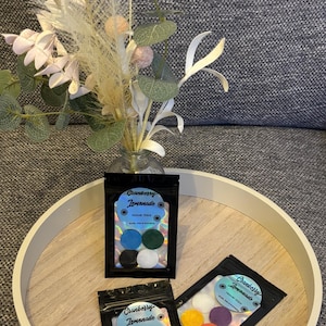 May include: Three black pouches of Hoover Discs with the text "Cranberry Lemonade" and various coloured discs. The pouches are on a white tray with a floral arrangement in a glass vase.