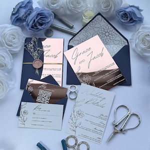 Puede incluir: Juego de invitaciones de boda con detalles en oro rosa, sobres azul marino y diseños florales. Las invitaciones incluyen los nombres "Grace and Jacob" y "Wedding Details". Incluye anillos, tijeras y rosas.