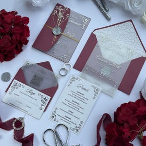 May include: Elegant wedding invitation suite featuring burgundy envelopes and translucent cards with silver accents. Includes RSVP, details, and invitation cards. The invitation cards have the names "Bennett & Wolfe" and "Licia & Cassian Wolfe".