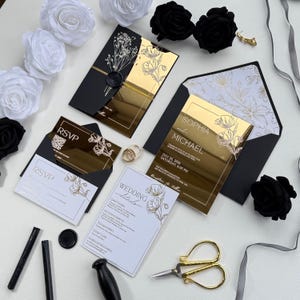 Op de afbeelding: Een elegante trouwuitnodigingssuite met goudkleurige spiegelkaarten, zwarte enveloppen en RSVP-kaarten. De uitnodiging bevat de namen "SOPHIA" en "MICHAEL" en de datum "20 juli 2006". Decoratieve elementen zijn witte en zwarte rozen.