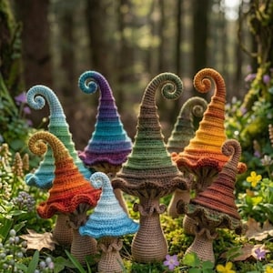 Puede incluir: Una colección de figuras de hongos de ganchillo coloridas con puntas rizadas. Los hongos presentan una variedad de colores, incluyendo azul, verde, naranja y morado. Se encuentran en un entorno natural al aire libre con follaje verde.