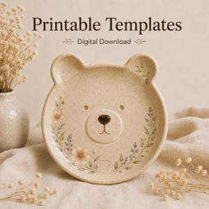 Könnte beinhalten: Eine beige, gesprenkelte, bärenförmige Keramikschale mit einem Blumenkranz-Design aus kleinen rosa und blauen Blüten, einer dunkelbraunen Nase und einem kleinen Herzsymbol. Der Text Printable Templates Digital Download steht über der Schale.