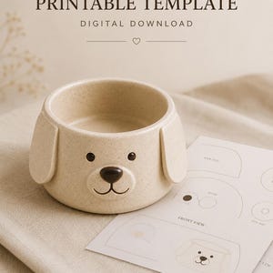 Könnte beinhalten: Eine beige, gesprenkelte Keramikschale in Hundeform mit Schlappohren, einer dunkelbraunen Nase und schwarzen Augen. Daneben liegt ein weißes Blatt Papier mit der Aufschrift PRINTABLE TEMPLATE DIGITAL DOWNLOAD und Diagrammen für EAR, NOSE, FRONT VIEW und EYE.
