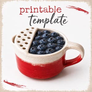 May include: A ceramic cup with a red base and a cream-colored top, filled with blueberries. The cup has a handle and a perforated section. The words "printable template" are written in red and black.