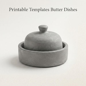 Puede incluir: Una mantequera gris con tapa. El plato es redondo y está hecho de un material sólido, con un diseño minimalista. El texto "Printable Templates Butter Dishes" está en la parte superior de la imagen.