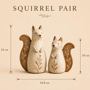 Op de afbeelding: Een paar crèmekleurige eekhoornbeeldjes met bruine spikkels en bloemmotieven op hun staarten en lichamen. De tekst SQUIRREL PAIR staat bovenaan. De afmetingen zijn aangegeven als 14 cm en 10 cm hoog, met een breedte van 14,8 cm.