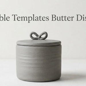 Puede incluir: Una mantequera de cerámica gris con tapa y asa en forma de lazo. El plato es cilíndrico con una superficie texturizada. El texto "Printable Templates Butter Dishes" está en la parte superior de la imagen.