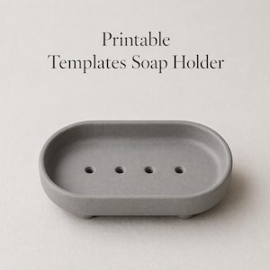 Może przedstawiać: Szary owalny mydelniczka z trzema małymi nóżkami i czterema otworami drenażowymi. Tekst "Printable Templates Soap Holder" jest wydrukowany nad mydelniczką. Ten minimalistyczny design jest odpowiedni do łazienki.