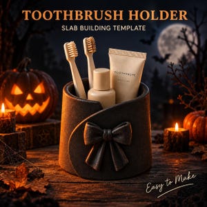 May include: A dark grey cylindrical toothbrush holder featuring a sculpted bow on the front. The holder contains two light-coloured toothbrushes, a small beige bottle, and a tube labelled TOOTHPASTE. Text reads TOOTHBRUSH HOLDER SLAB BUILDING TEMPLATE.
