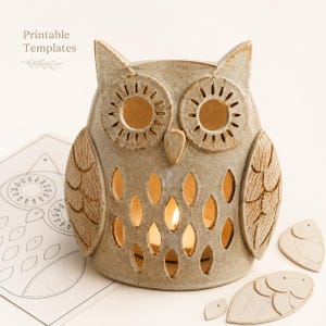 May include: A beige ceramic owl-shaped candle holder with cut-out eye and feather patterns, illuminated from within. Beside it lies a paper sheet labeled Printable Templates and several small, detached paper cut-out shapes of owl feathers.