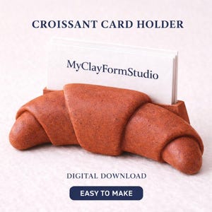May include: A terracotta-colored croissant-shaped card holder. The holder is designed to cradle a stack of white business cards, with the text "MyClayFormStudio" visible. The words "CROISSANT CARD HOLDER" are at the top, and "EASY TO MAKE" is at the bottom.