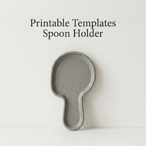 May include: A grey ceramic spoon rest with a rounded top and a handle. The text "Printable Templates Spoon Holder" is printed in black above the spoon rest. The spoon rest is designed to hold a spoon while cooking.