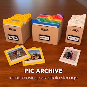 May include: Photo storage boxes with labeled tabs and photo frames. The boxes are beige with labels reading "2026", "Mom's Day", and "My Love". The photo frames are yellow and white, each holding a photo.