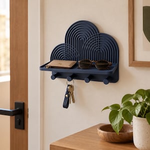 Puede incluir: Un organizador de pared azul oscuro con un panel trasero en forma de nube y patrones de arcos concéntricos. La unidad incluye un estante plano con una cartera beige y gafas de sol marrones, además de cuatro ganchos cilíndricos para llaves.