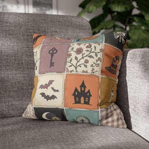 May include: A square throw cushion featuring a patchwork design with various Halloween-themed illustrations. The grid pattern includes a skeleton, a witch hat, a haunted house, bats, a key, a candle, a crescent moon, a tombstone, and floral motifs.