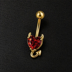 Può includere: Anello per ombelico color oro con un design a tema diavolo. L'anello presenta una gemma rossa a forma di cuore con piccole corna e una coda. La sfera superiore e l'anello stesso sono dorati, su sfondo nero.
