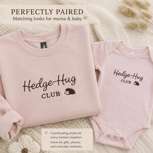 May include: A light pink long-sleeve sweatshirt and a matching short-sleeve baby bodysuit. Both garments feature dark brown embroidered text that reads Hedge-Hug CLUB with a small hedgehog graphic. The set is designed for coordinated outfits.