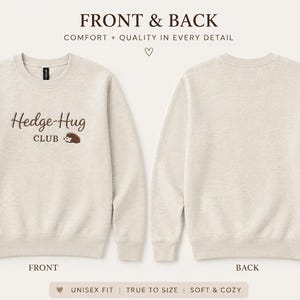 May include: A beige crewneck sweatshirt featuring the brown text Hedge-Hug CLUB and a small brown hedgehog graphic on the front. The back of the sweatshirt is plain beige. The text FRONT & BACK and COMFORT + QUALITY IN EVERY DETAIL appear above.