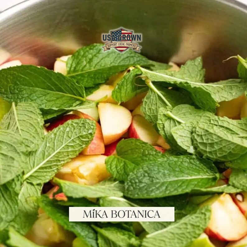 Puede incluir: Primer plano de un cuenco lleno de rodajas de manzana y hojas de menta verde. La imagen presenta el texto "USA Grown Support Local Farmers" y "M&iacute;ka Botanica".