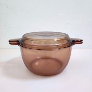 Op de afbeelding: Een amberkleurige glazen ovenschaal met bijpassende deksel. De schaal heeft twee handvatten aan de zijkant en een afgeronde vorm. De deksel is transparant. Geschikt voor bakken en serveren.