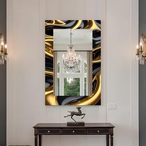 May include: A rectangular mirror with a swirling gold, black, and gray frame hangs above a dark wood console table. The mirror reflects a chandelier and a window. A bronze deer sculpture sits on the table. The room has white paneling and sconces.