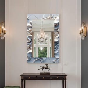 Può includere: Uno specchio rettangolare con un design astratto strutturato in tonalità di grigio e bianco è appeso sopra una consolle in legno scuro. Lo specchio riflette un lampadario e una finestra. Una scultura di cervo in bronzo è sulla tavola.