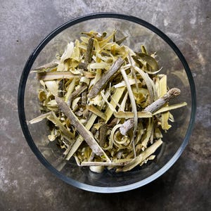 May include: A clear glass bowl filled with a collection of dried, light yellow and brown woody plant strips and small twigs. The pieces vary in length and thickness, featuring a fibrous texture and a mix of pale cream and earthy brown tones.