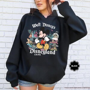 Pu&ograve; includere: Felpa con cappuccio nera con una grafica di Topolino a Disneyland. Il design include il testo "Walt Disney's Disneyland Est. 1955". La felpa ha una tasca frontale e un cappuccio con coulisse.