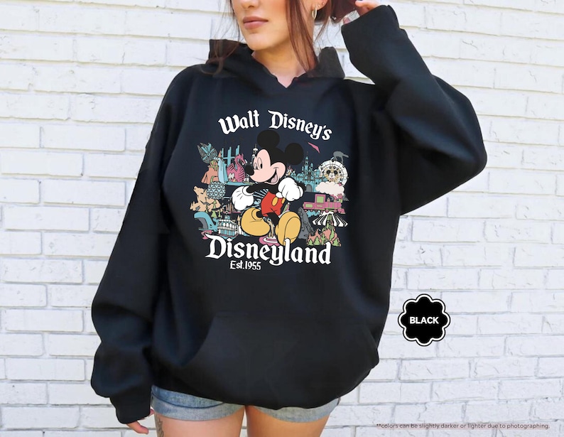 Pu&ograve; includere: Felpa con cappuccio nera con una grafica di Topolino a Disneyland. Il design include il testo "Walt Disney's Disneyland Est. 1955". La felpa ha una tasca frontale e un cappuccio con coulisse.