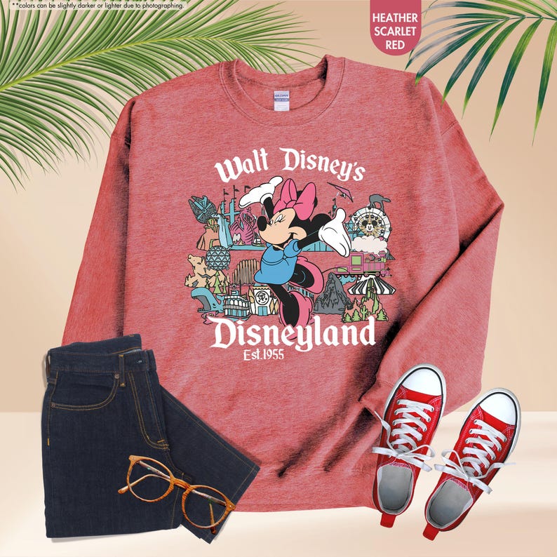 Pu&ograve; includere: Felpa rosso scarlatto melange con grafica di Minnie Mouse e la scritta "Walt Disney's Disneyland Est.1955". L'immagine include anche jeans blu scuro, scarpe da ginnastica rosse e occhiali.