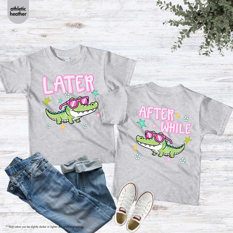 May include: Two athletic heather gray t-shirts with a cartoon alligator wearing pink sunglasses. One shirt says "LATER" and the other says "AFTER WHILE". The shirts are paired with blue jeans and white sneakers.