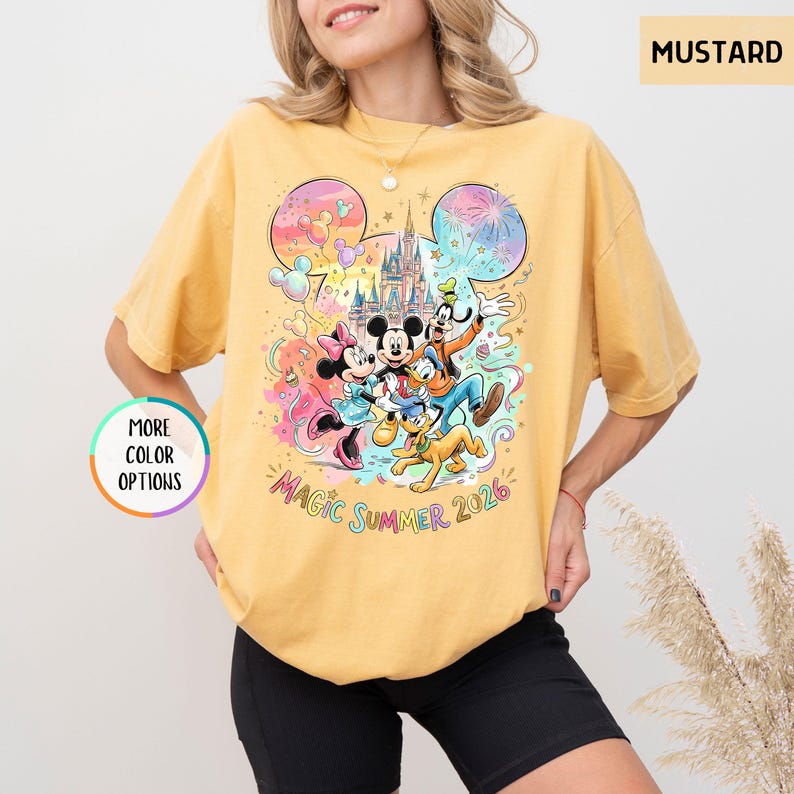 K&ouml;nnte beinhalten: Senffarbenes T-Shirt mit einer farbenfrohen Grafik von Disney-Figuren, darunter Micky und Minnie Maus, Goofy und Donald Duck, mit einem Schloss und Feuerwerk. Der Text "Magic Summer 2026" ist ebenfalls sichtbar.