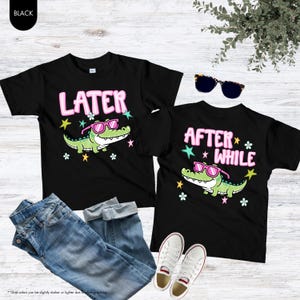 May include: Two black t-shirts with alligator graphics wearing sunglasses and the phrases "LATER" and "AFTER WHILE" in pink. The shirts are paired with blue jeans and white sneakers.